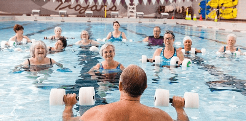 Adult doing water aerobics in a pool, with the instructor in the foreground facing away from the camera.