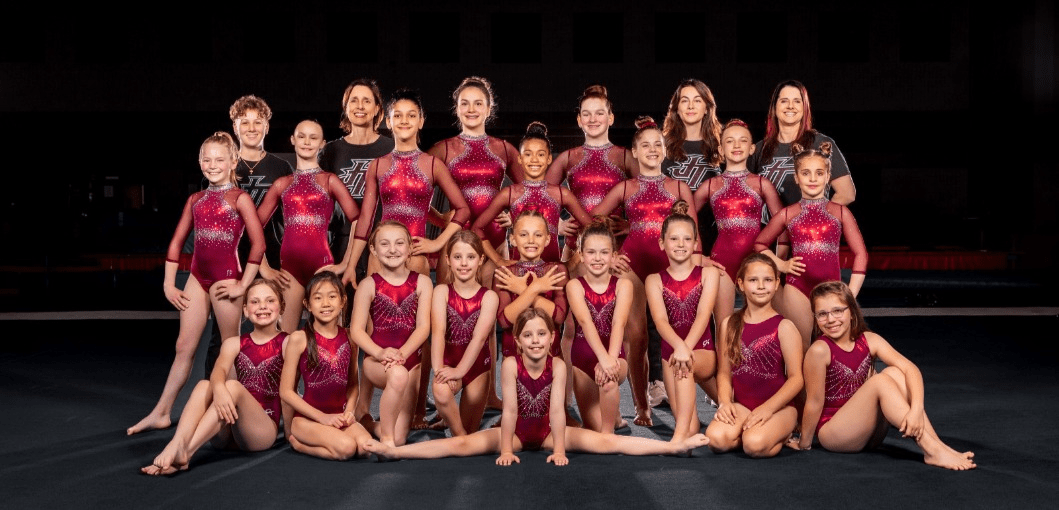 JT Gymnastics team posed in leotards with coaches