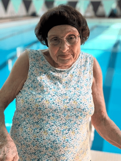 Alma Churchill, a white woman with short brown hair and glasses standing in front of a swimming pool.