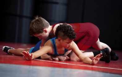 Two boys wrestling on a mat.