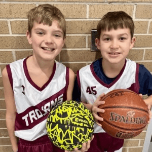 Boys holding basketballs in white Trojans jerseys.