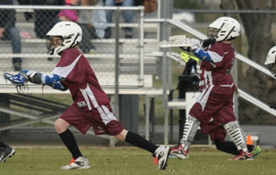 Jenks youth lacrosse boys running on field in uniform.
