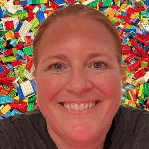 Kim Dammann, a white woman with hair pulled back in front of a pile of LEGOs.
