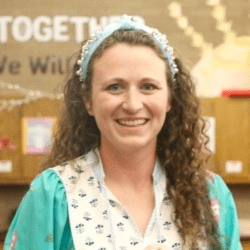 Macy Worley, a woman with long, curly brown hair, wearing a teal outfit, standing in her classroom.