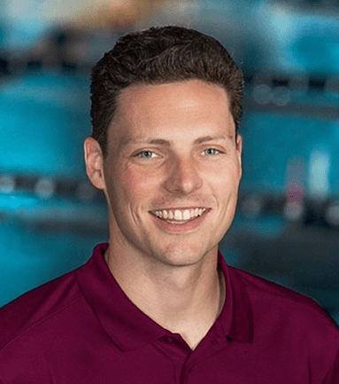 A smiling man with short brown hair, wearing a maroon polo shirt with a pool in the background.
